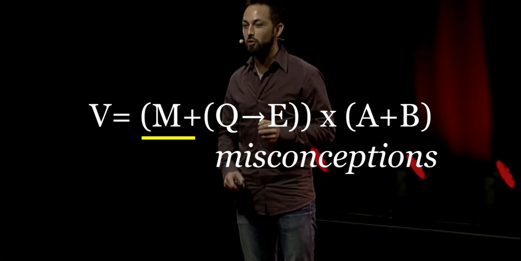 Derek Muller speaking onstage beneath a mnemonic formula with misconceptions highlighted